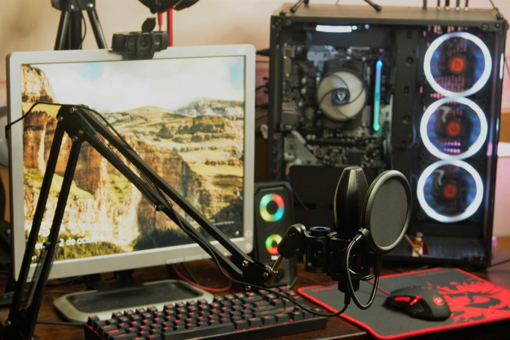 A sleek gaming and recording setup featuring a microphone, monitor, and RGB-lit PC case.